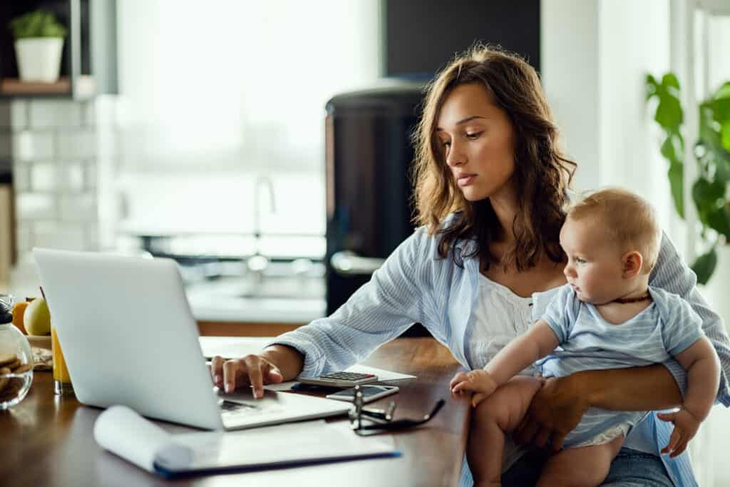 Kobieta z dzieckiem przy laptopie planująca urlop macierzyński w pracy